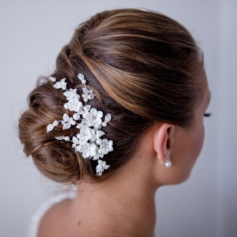 A pretty floral wedding hair clip featuring delicate ivory porcelain flowers nestled amongst sprays of glistening crystal embellished leaves and ivory faux pearls.